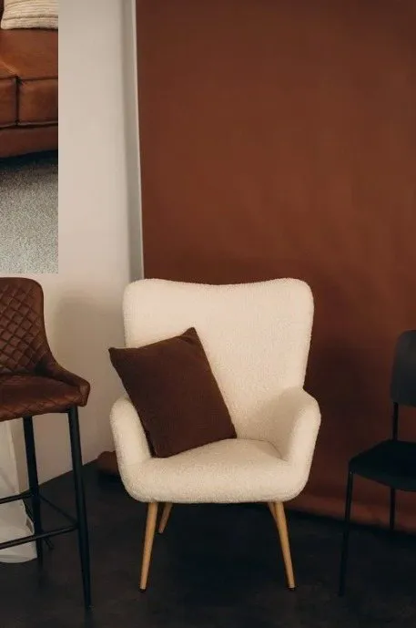 Balts mīksts krēsls ar brūnu spilvenu pie brūna papīra fona fotostudijā